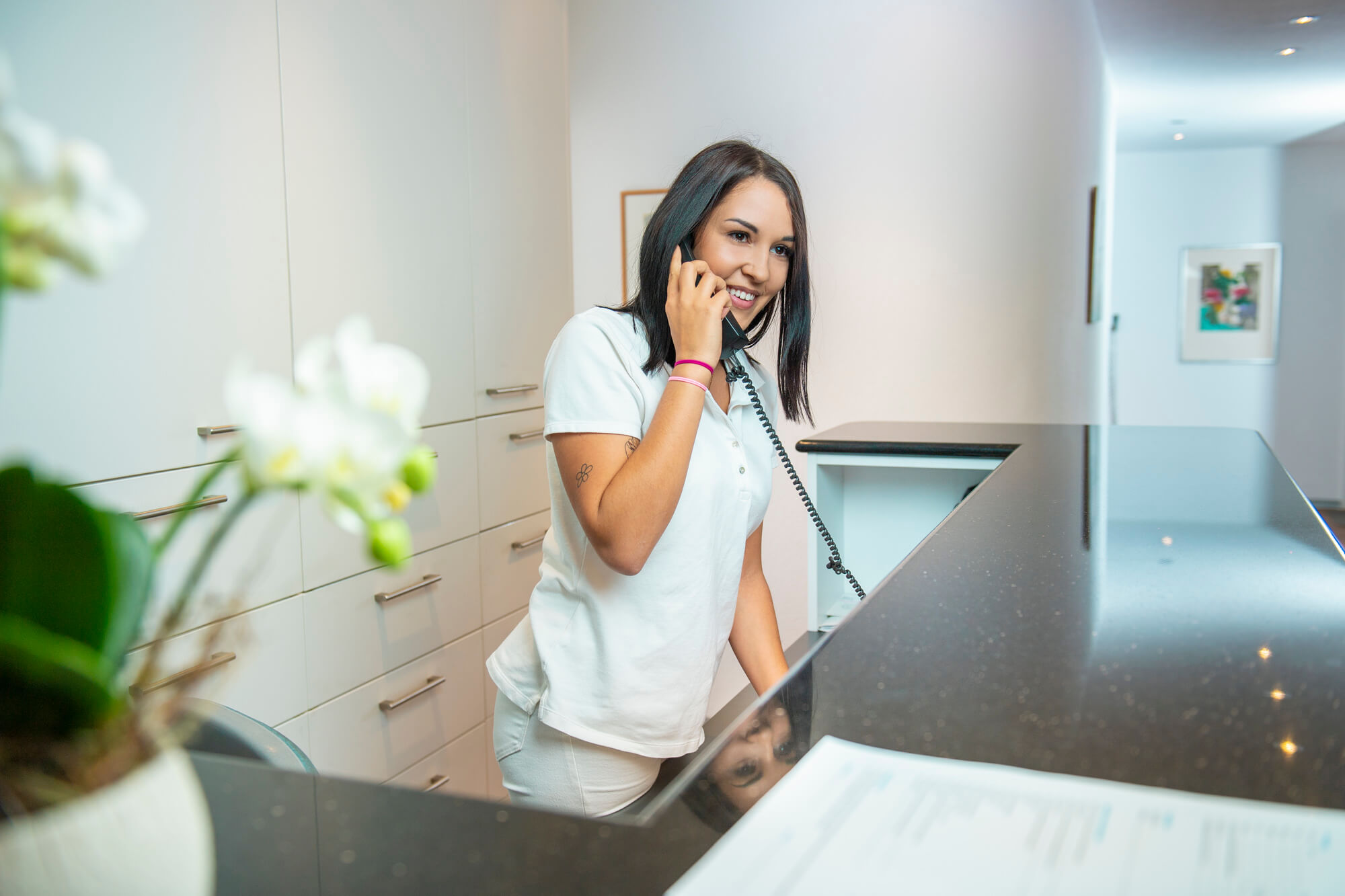 Mitarbeiterin am Telefon hinter dem Empfangstresen mit Blumen im Vordergrund